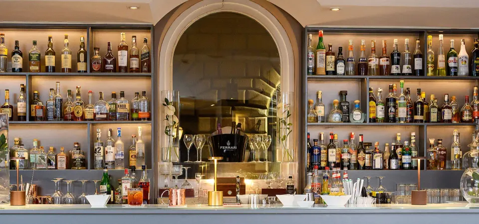 Hotel bar with backlit shelves of bottles and an arched stone niche